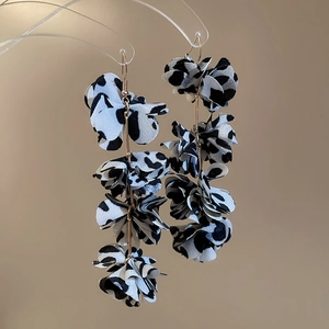 Close-up of dangling fabric flower earrings with black and white cow print and gold hooks