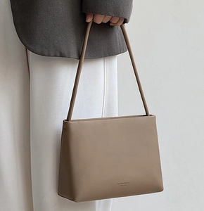 Detailed view of the khaki trapezoid leather handbag with a slim shoulder strap on model