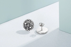 Macro shot of silver tree of life earrings with secure butterfly backings on blue background