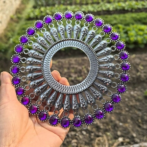 Detail of silver metal round wall decor featuring inlaid purple beads held in a garden