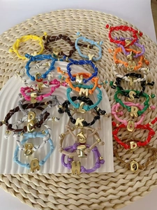 Detailansicht von 26 bunten geflochtenen Armbändern mit goldenen Buchstaben-Anhängern