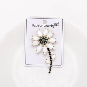 Detail of a gold floral brooch with white petals and black rhinestones on a card