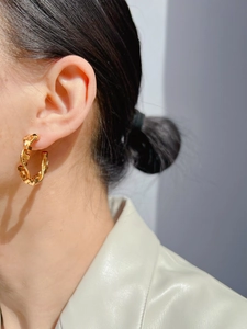 Close-up of golden C-shaped hoop earring with snake-skin texture worn by a model