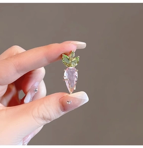 Macro shot of pink crystal carrot brooch with green leaves and faceted metal finish