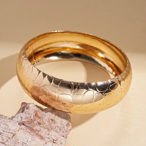 Macro shot of gold wide bangle with crocodile pattern on natural stone display