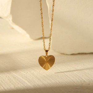 Detailed view of heart-shaped gold pendant with radial texture on beige background