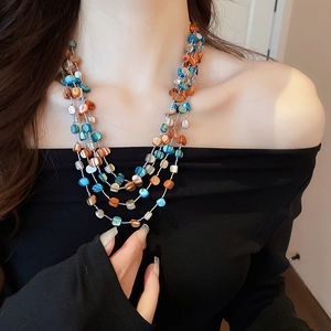 Detail of layered necklace with irregular orange, blue and white shell beads on model