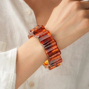 Close-up of amber tortoiseshell wavy resin bangle worn over a white linen shirt