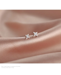 Detail of S925 sterling silver four-point star earrings on smooth pink silk fabric
