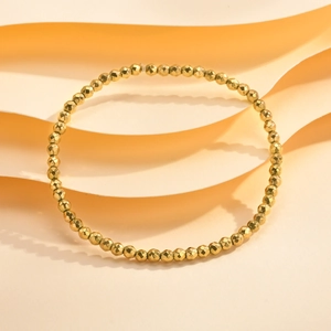 Macro detail of gold faceted bead bracelet on a textured beige minimalist background