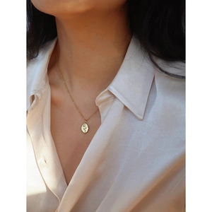 Close-up of a gold oval rose flower relief pendant on a minimalist stainless steel chain