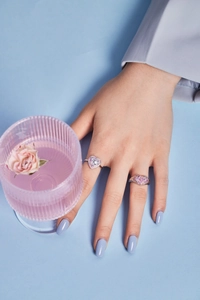 Close-up of heart-shaped silver rings with pink and purple zircon stones on a hand