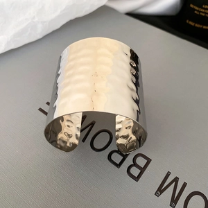 Detailed view of wide silver metal cuff bangle featuring modern hammered texture finish