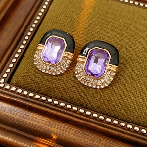Detailed close-up of vintage gold enamel earrings with purple crystals on green velvet
