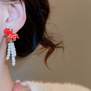 Detail of red enamel pony earrings with pearl tassels on a model for a luxury look