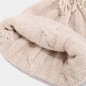 Detailed close-up of chunky knit cable pattern and ribbed texture on beige winter hat
