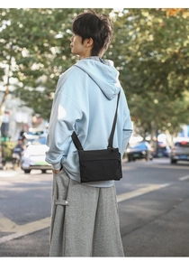 Close-up of minimalist black nylon crossbody bag on model in an urban street setting