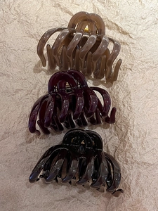 Close-up of three large acrylic hair claw clips in amber, burgundy and black colors