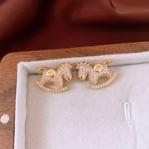 Detail of gold rocking horse stud earrings with zircon inlay on luxury velvet display