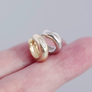 Macro shot of gold and silver huggie earrings with marquise-cut cubic zirconia on fingertips