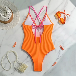 Detail of orange ribbed one-piece swimsuit with pink lace-up back on marble surface