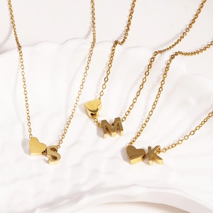 Detailed shot of 18k gold plated stainless steel heart and initial pendants on a shell plate