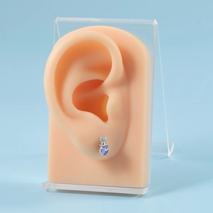Detailed view of a silver heart-shaped earring with purple zircon on a model ear