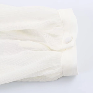 Detailed close-up of white ruffled cuff with elegant button on layered chiffon shirt