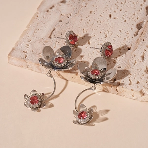 Detailed macro view of silver flower earrings with red zircon stones on beige travertine