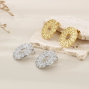 Close-up of gold and silver oval woven earrings on a textured stone surface