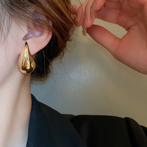Close-up of elegant gold teardrop earring worn by a model in soft natural lighting