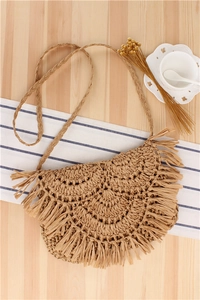 Detail of semi-circular woven straw crossbody bag with fringe on a rustic wooden background