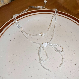 Detail of double-layered beaded necklace with heart and bow pendants on a ceramic plate