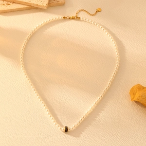 Detail of white pearl necklace with gold clasp and central black bead on beige leather