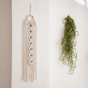 Detail of woven cotton wall hanging with blue evil eye beads and natural tassels