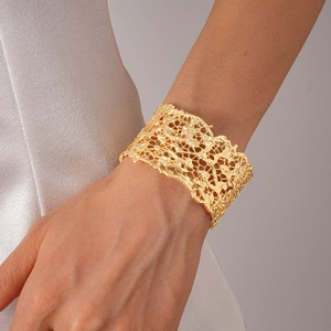 Detail of wide gold cuff bracelet featuring intricate lace cutout patterns on the wrist