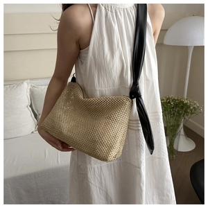 Detail of woven straw tote bag with black leather knotted shoulder strap on white dress