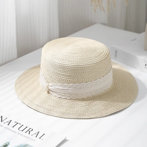 Straw hat with white lace ribbon and pearl accent on a minimalist white background