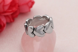 Detailed macro shot of silver heart-shaped bead ring resting on a pink pebble background