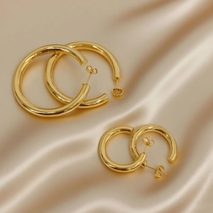 Detailed view of two pairs of gold-plated hoop earrings on luxury silk background