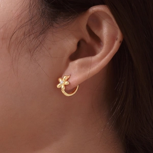 Detailed view of gold flower earrings with central zircon stone on model's ear