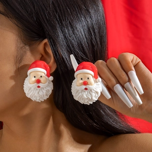 Gros plan d'une boucle d'oreille Père Noël en résine avec bonnet rouge sur fond de fête