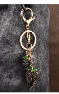 Macro detail of golden metal keychain with black strawberry pendants and green leaves