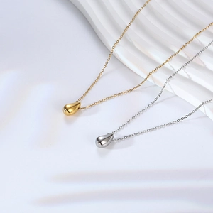 Collane con ciondolo a goccia minimaliste in oro e argento su sfondo ondulato