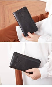 Detail showing handheld black leather passport holder with elastic band and embossed logo