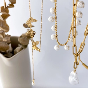 Detail of layered gold necklaces with butterfly charm, paperclip links, and baroque pearls
