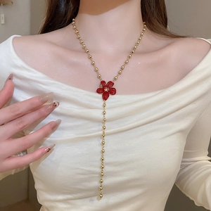 Detailed view of long gold beaded necklace with a red flower pendant worn by a model