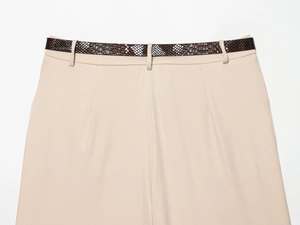 Gros plan d'un pantalon sergé beige avec une ceinture texturée en peau de serpent marron