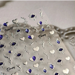 Close-up of gothic nail stickers featuring silver embossed hearts and purple eye designs