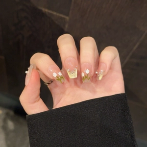 Détail d'ongles peints avec tulipes, perles et paillettes dorées sur base rose